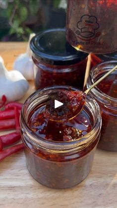 some jars filled with food sitting on top of a wooden table next to garlic and red peppers