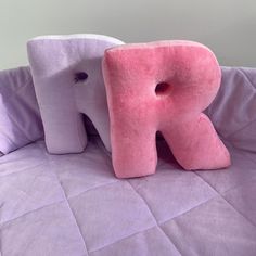 two pink and white elephant pillows sitting on top of a purple bed sheet with the letter k