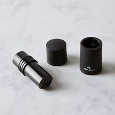 two black containers sitting on top of a white counter next to an empty container with a lid