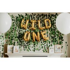 some balloons that say wild one are in front of a fireplace with ivy on the wall