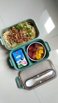 a lunch box with noodles, meat and fruit in it on a white countertop