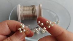 two hands are holding some pearls and thread