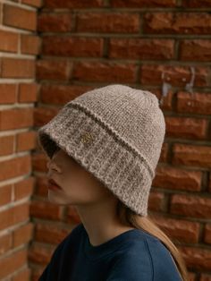 a woman wearing a knitted hat standing in front of a brick wall with her head turned to the side