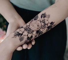 a woman's arm with flowers and a full moon tattoo on her left arm