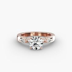 a rose gold engagement ring with three stones on the side and a round brilliant diamond center