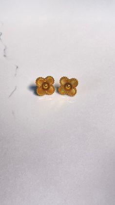 two gold earrings sitting on top of a white surface