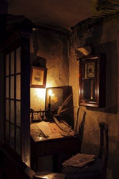 an old desk in the corner of a room with a lamp on it and pictures hanging up