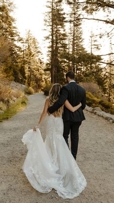 a bride and groom walking down a path in the woods