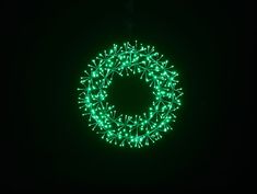 a green wreath is lit up in the dark, with lights on each side and around it