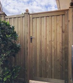 a wooden gate in front of a green bush and blue sky with clouds above it