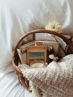 a wicker basket filled with books sitting on top of a white sheet covered bed