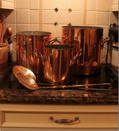 copper pots and pans are sitting on the kitchen counter top with utensils