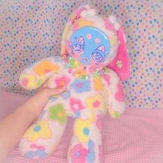 a hand holding a colorful stuffed animal on top of a pink and white bed sheet