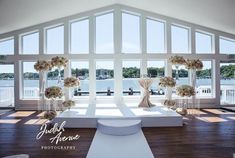 a large room with white furniture and flowers on the tables in front of windows that look out onto water