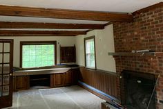 an empty living room with brick fireplace and wood paneling