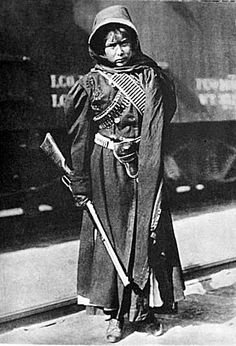 an old black and white photo of a woman with a long coat, holding a cane