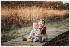 two young children sitting on a wooden bridge