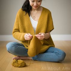 a woman is sitting on the floor and knitting with her hands while wearing a yellow knitted shawl