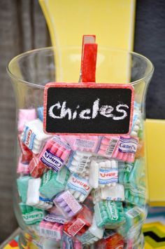 a glass filled with lots of candy sitting next to a chalkboard on top of a table