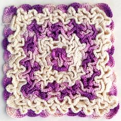 a crocheted square with white and purple squares on the bottom, in front of a white background