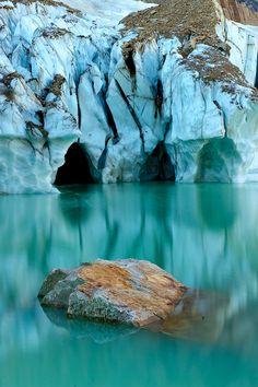 a large rock sitting in the middle of a body of water near an ice cave