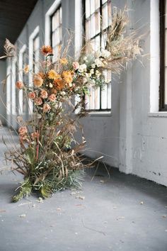 an arrangement of flowers is sitting on the floor in front of a window and wall