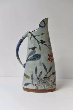 a ceramic pitcher with birds and flowers on it's side, sitting on a white surface