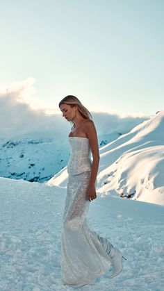 a woman in a white dress walking through the snow