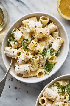 two bowls filled with pasta and vegetables next to sliced lemons on a marble surface