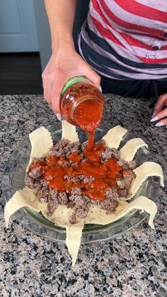 a person pouring sauce on food in a glass bowl sitting on top of a counter