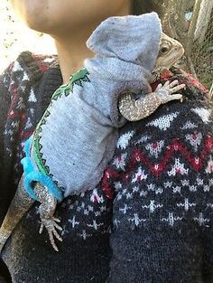 a woman holding a small lizard on her back while wearing a sweater with an attached collar