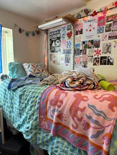 an unmade bed in a bedroom with posters on the wall and windows above it