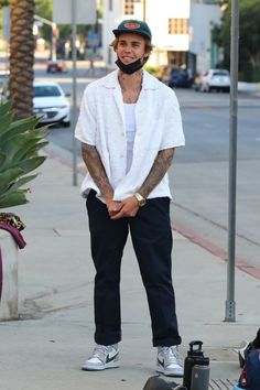 a man standing on the sidewalk with his skateboard next to him and wearing a bandana