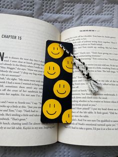 a bookmark with smiley faces on it sitting in front of an open page of a book