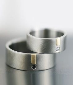 two wedding rings with diamonds on them sitting on a table together, one is silver and the other is gold