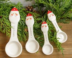 four spoons with santa claus faces on them are sitting in front of pine branches