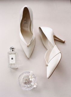 a pair of white high heels next to a perfume bottle