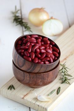 a wooden bowl filled with red beans on top of a cutting board next to an onion