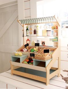 a wooden toy kitchen with food in the drawer and on the shelf next to it