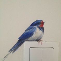 a painting of a blue bird sitting on top of a white light switch cover in a room