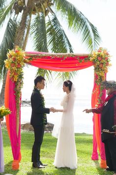 a couple getting married under an orange and pink wedding arch