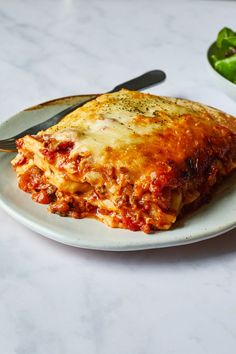 a slice of lasagna on a plate with a fork and salad in the background