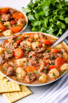 two bowls filled with stew next to crackers and parsley