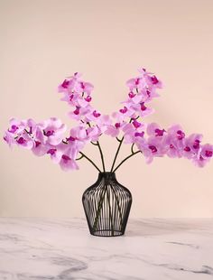 a black vase filled with pink flowers on top of a marble countertop next to a white wall