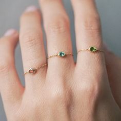 a woman's hand wearing a gold ring with green stones on the middle finger