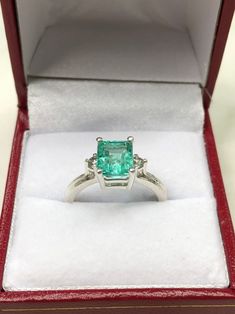 Displayed is a classic Colombian emerald three stone emerald-cut engagement ring in .925 sterling silver. This gorgeous ring carries a full 2.0-carat emerald in a four prong setting. Fully faceted, this gemstone showcases excellent shine. The emerald has excellent clarity with minor flaws that are normal in all genuine emeralds but no carbon spots (black) or harsh flaws are found in this beauty! The gem has a light green color and excellent luster. Two natural diamonds accent the emerald. An ide Three-stone Fine Jewelry For Proposal, Fine Jewelry Three Stone For Proposal, Three Stone Fine Jewelry For Proposal, Green Three Stone Emerald Cut Jewelry, Emerald Cut Three Stone Birthstone Ring, Emerald Cut Center Stone Jewelry For Proposal, Emerald Cut Jewelry With Center Stone For Proposal, Gift Emerald Ring With Three Stones In Radiant Cut, Radiant Cut Emerald Ring In Sterling Silver For Wedding