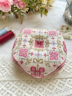 a needle case sitting on top of a table next to pink flowers and thread spools