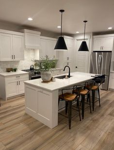 a large kitchen with white cabinets and black pendant lights hanging from the ceiling over the island