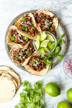 several tacos on a plate with limes and cilantro next to them