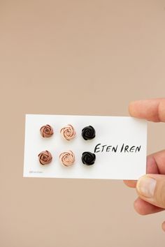 a hand holding a card with four small black and pink rosette studs on it